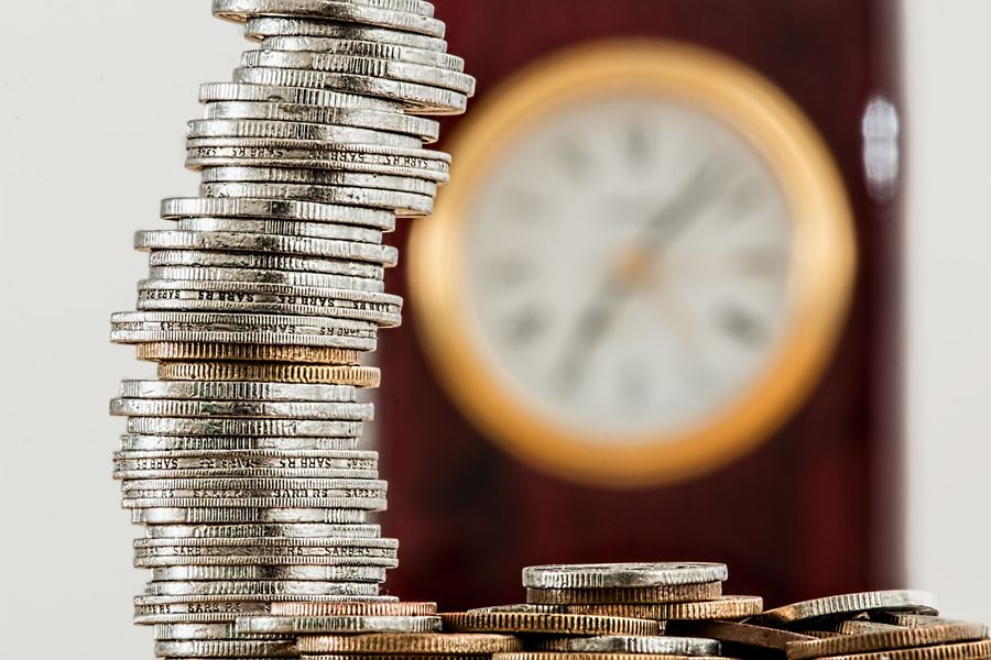 Pilha de moedas ao lado de um relógio, representando economia de tempo e recursos